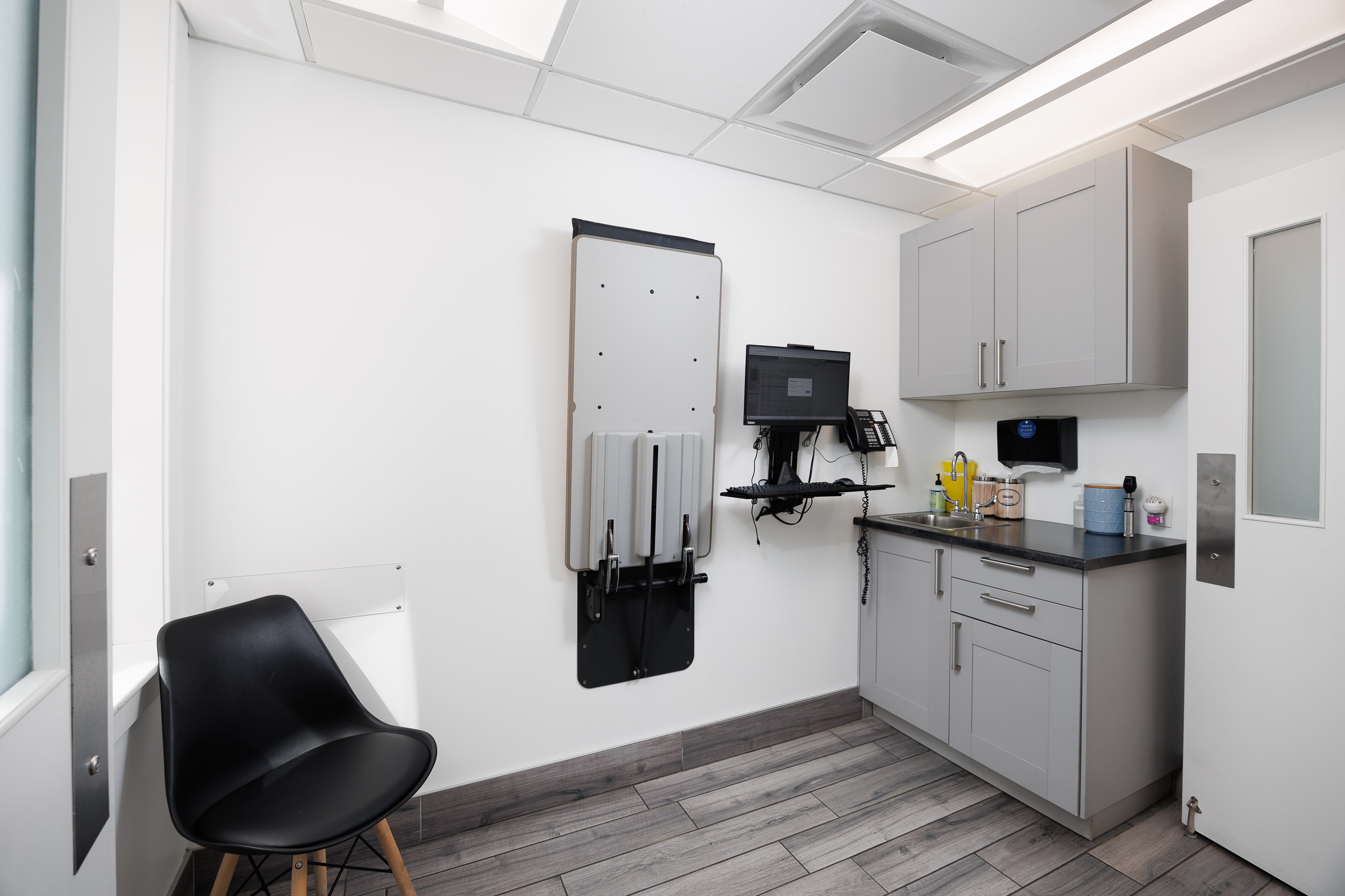 The image shows a well-lit dental office with modern equipment, featuring a dental chair, examination table, and various instruments.