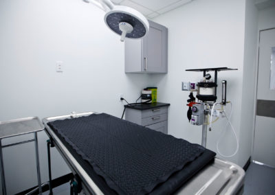 The image shows a small, well-equipped medical examination room with a black cloth covering the examination table.