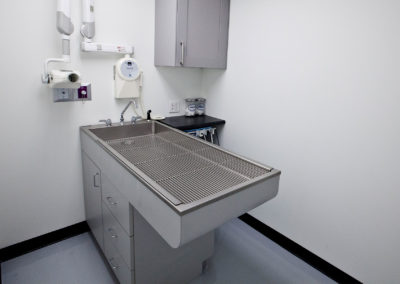 The image shows a small room with a stainless steel sink countertop and a metal sink basin, situated within a white cabinetry unit.