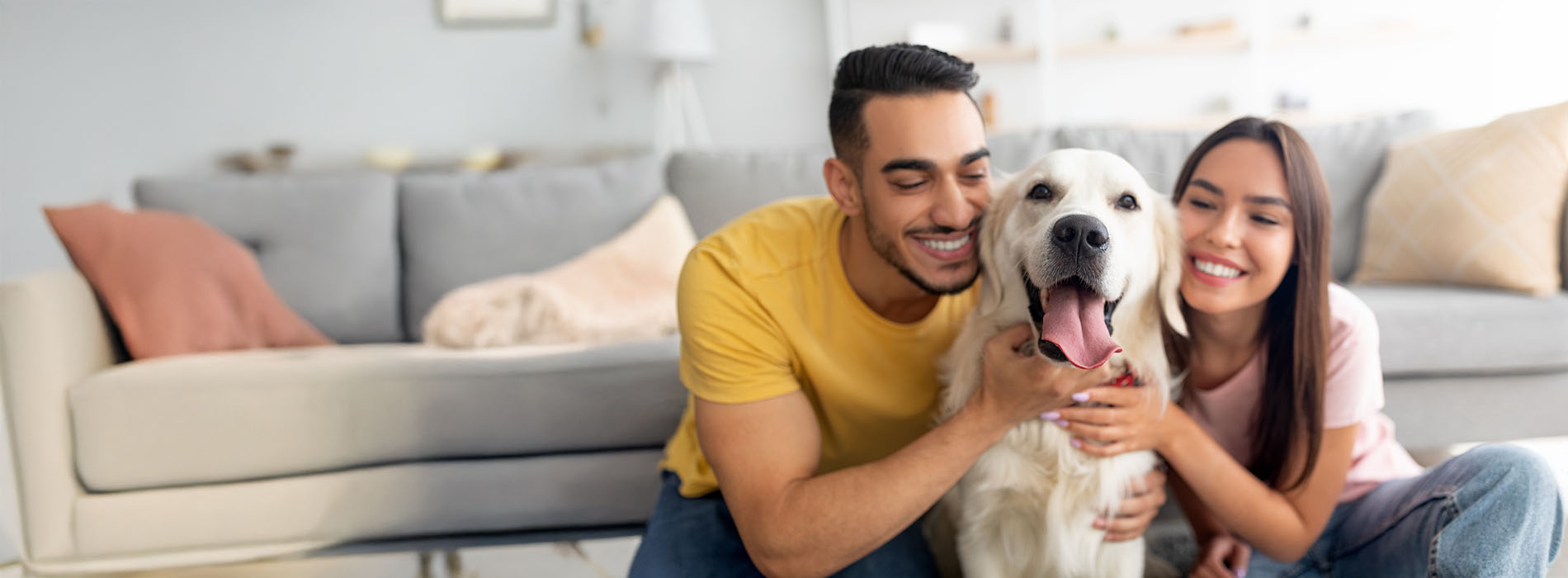 A young couple with a dog, posing together indoors, smiling at the camera.