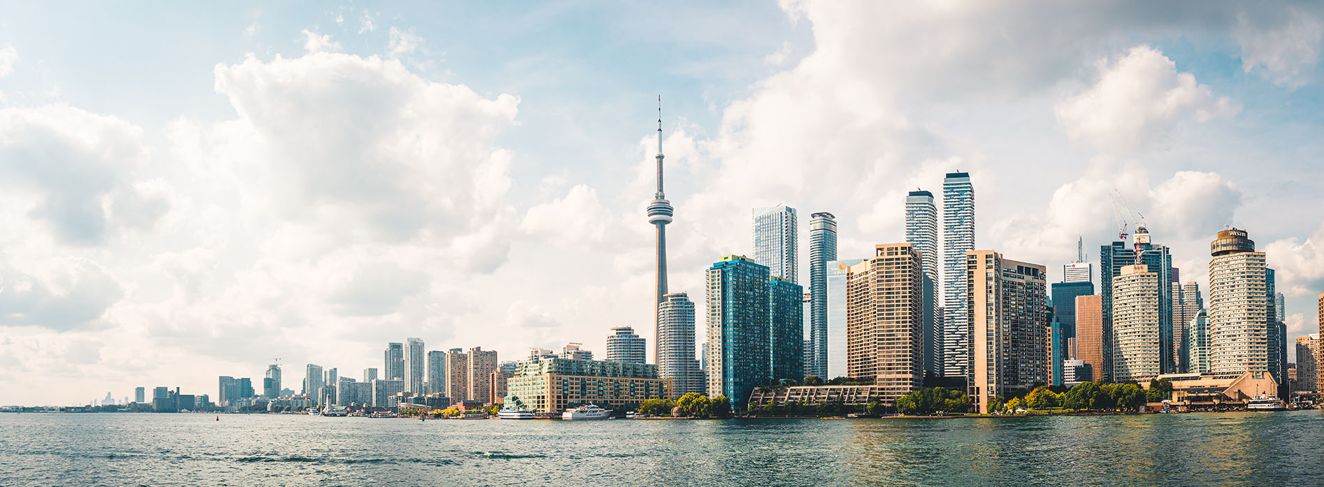 The image shows a scenic view of a city skyline with a prominent tower featuring an observation deck, flanked by a body of water, with a clear blue sky above and a few clouds scattered throughout.