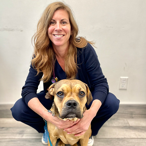 The image shows a woman kneeling down next to a large brown dog with its head resting on her shoulder, both posing for the photo.