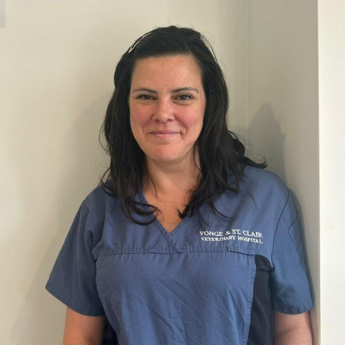 The image shows a woman wearing scrubs standing against a wall with a whiteboard behind her.